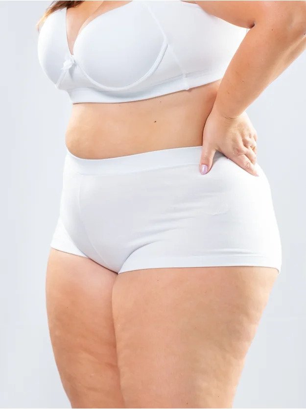 modelo de lado com mao na cintura com sutia e bodyshorts plus size em algodao branco