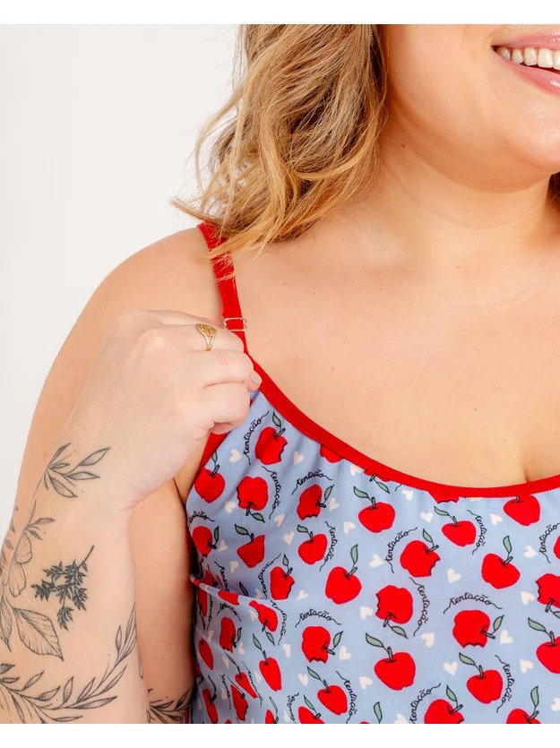 modelo  segurando alca do pijama estampado com macas em fundo azul claro com coracoes brancos e escrito tantacao nas frutas