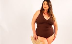 modelo usando maio plus size ariela chocolate estampado segurando leque de palha